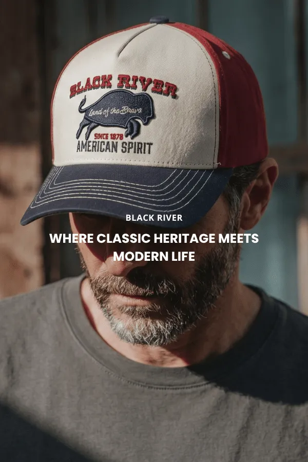 Un homme est assis sur une caisse en bois dans un studio et porte un chapeau de cowboy classique en feutre brun à large bord, une chemise en denim foncé et un jean.